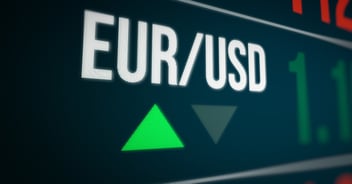 The characters EUR/USD appear, positioned at an oblique angle, against a black computer screen background, hovering above two arrowhead symbols, with a green one pointing upwards, and a greyed out one pointing downwards