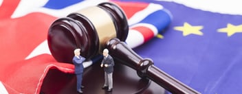 Two figurines discuss politics next to a large gavel lying on both a British and an EU flag