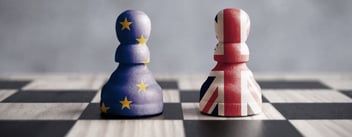 Two pawns stand alongside one another on a chessboard, one draped in the EU flag, the other in that of the United Kingdom