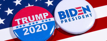 Against a diagonally positioned backdrop of the US flag, two electoral badges sit side by side, in an oblong fashion, with the one on the left displaying the red and white electoral logo of candidate Donald Trump, with the text 